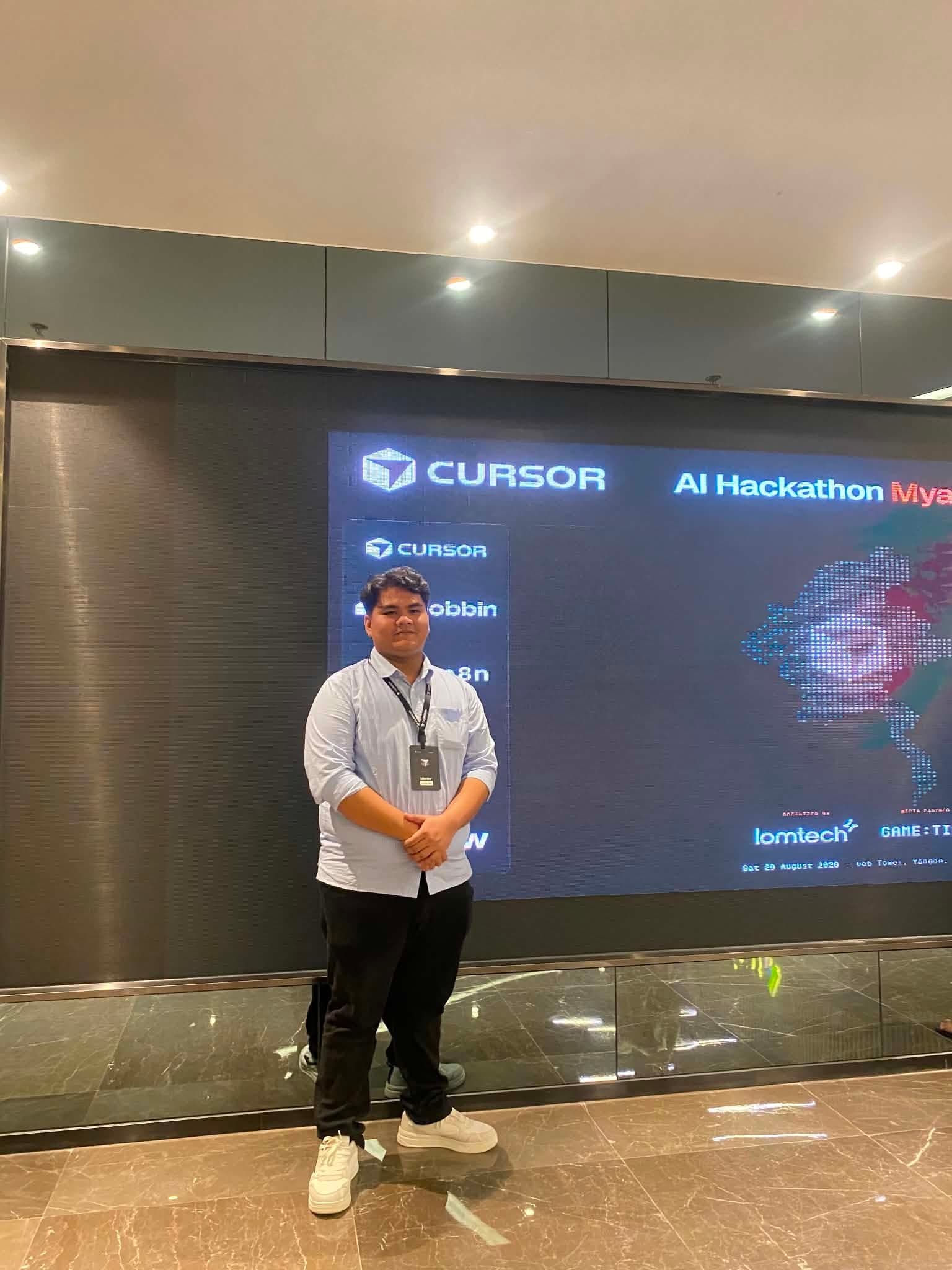 Aung Ye Htet standing as mentor in front of the Cursor AI Hackathon Myanmar backdrop at uab Tower, Yangon